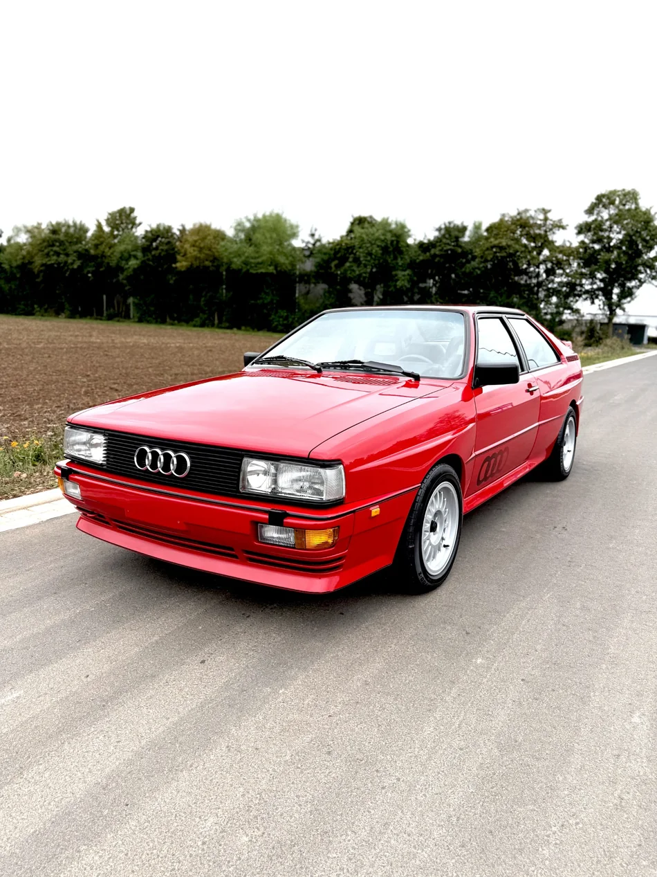Klassisches rotes Audi-Coupé mit silbernen Felgen auf einer Landstraße.