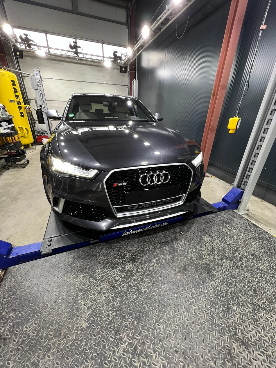 Dunkler Audi auf einer mit fahrzeugliebe.de beschrifteten Hebebühne in der Aufbereitung.