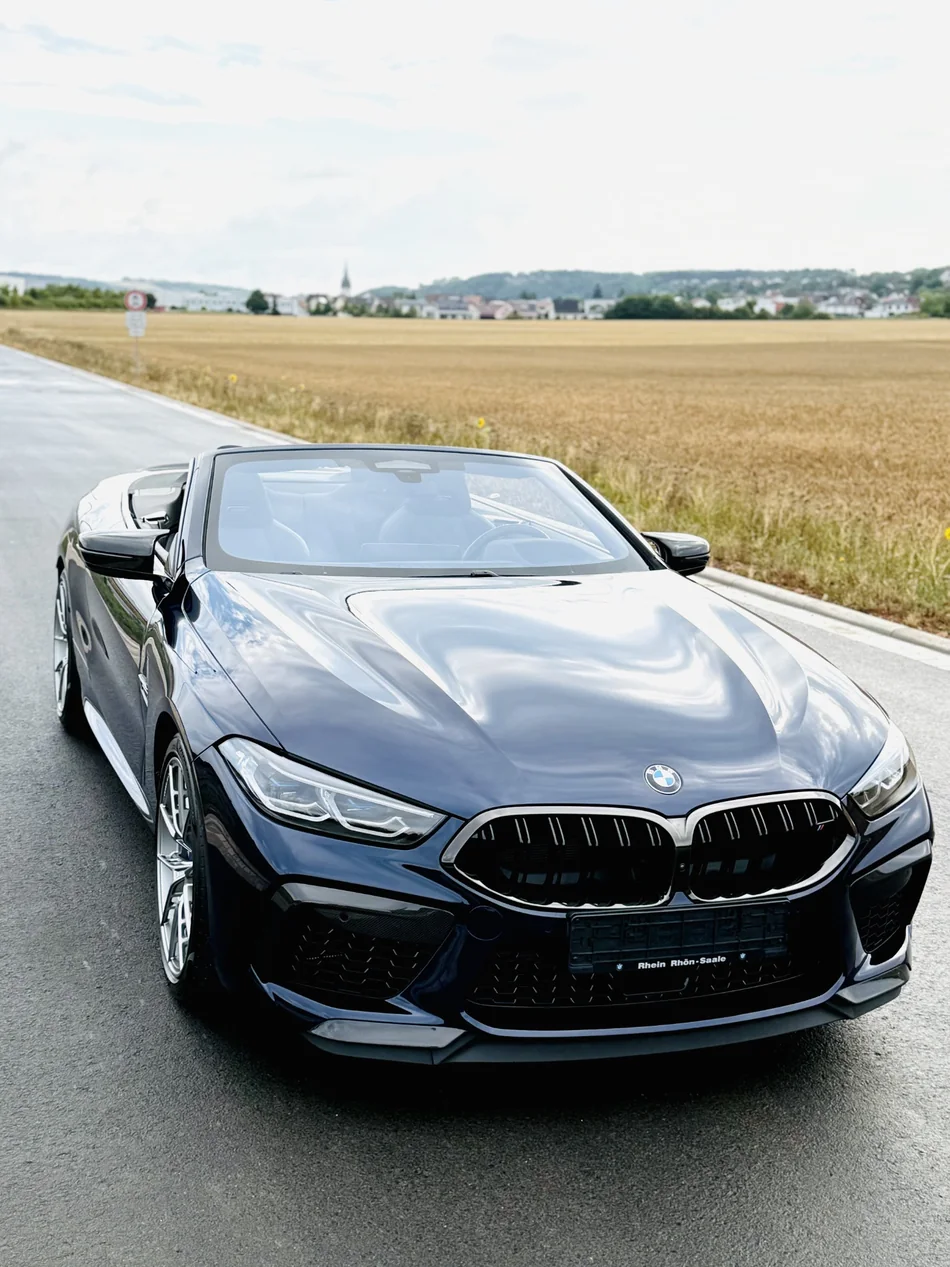 Dunkles BMW-Cabrio mit geöffnetem Dach und Spiegelungen auf der Motorhaube.