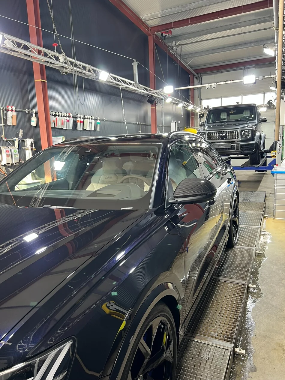 Audi-Kombi auf dem Aufbereitungsplatz mit Pflegeprodukten und einer Mercedes-G-Klasse im Hintergrund.
